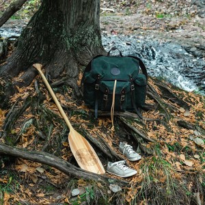 Duluth Pack Gitchi Gami Wanderer pack, wooden paddle and Astral shoes at the base of a tree