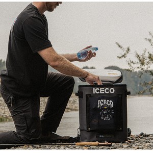 Man loading a bottle of water into an ICECO GOPACK12 portable fridge by a river