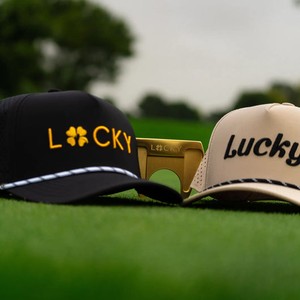 Black and tan Lucky Golf hats on a putting green with a gold Lucky putter